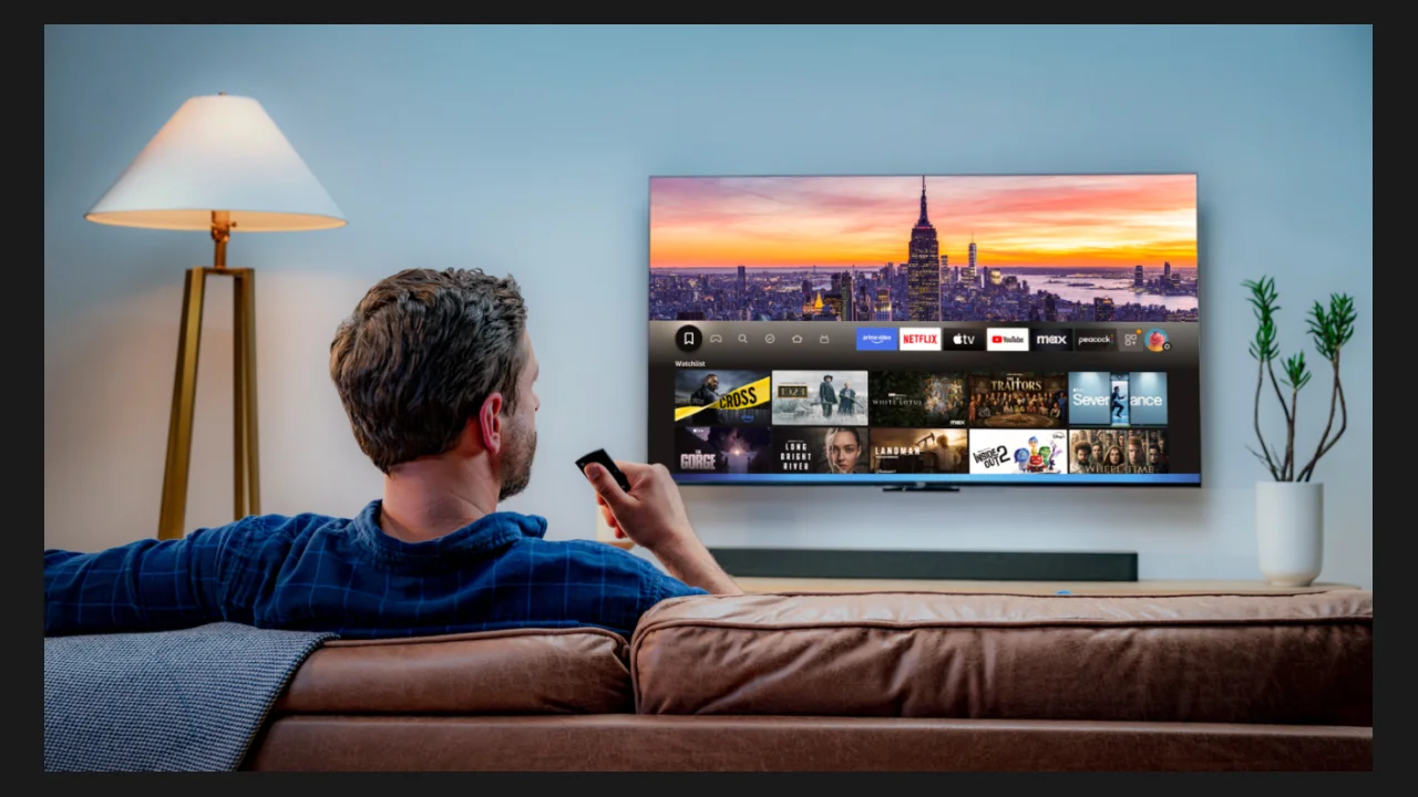 A man sitting on a sofa watching a television showing rows of movies