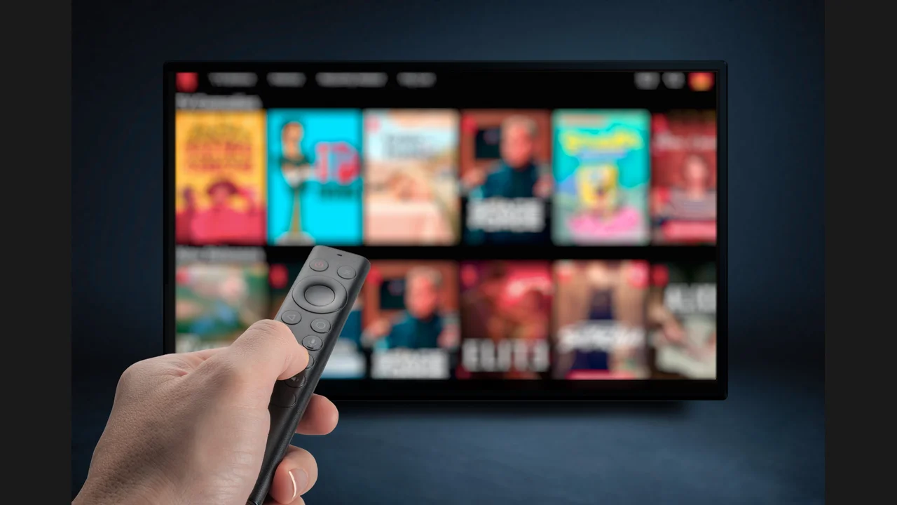 A hand holding a remote pointed at a television showing a grid of movie posters